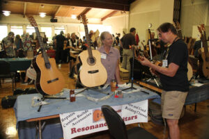 Teri Moore at Kevin Moore's Resonance Guitars display lets David Lawrence try out a uke. (Korsmo)